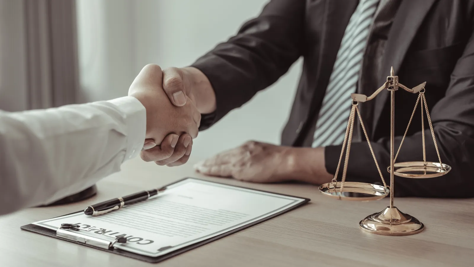Poignée de main au-dessus d'un contrat, à côté d'une balance de la justice